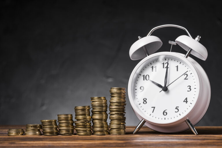 stack increasing coins with white alarm clock wooden desk against black background