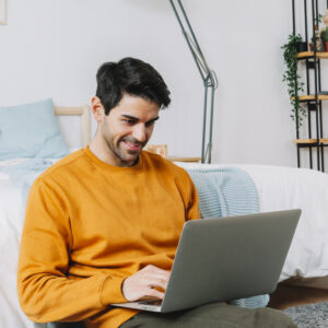 smiling man using laptop near bed